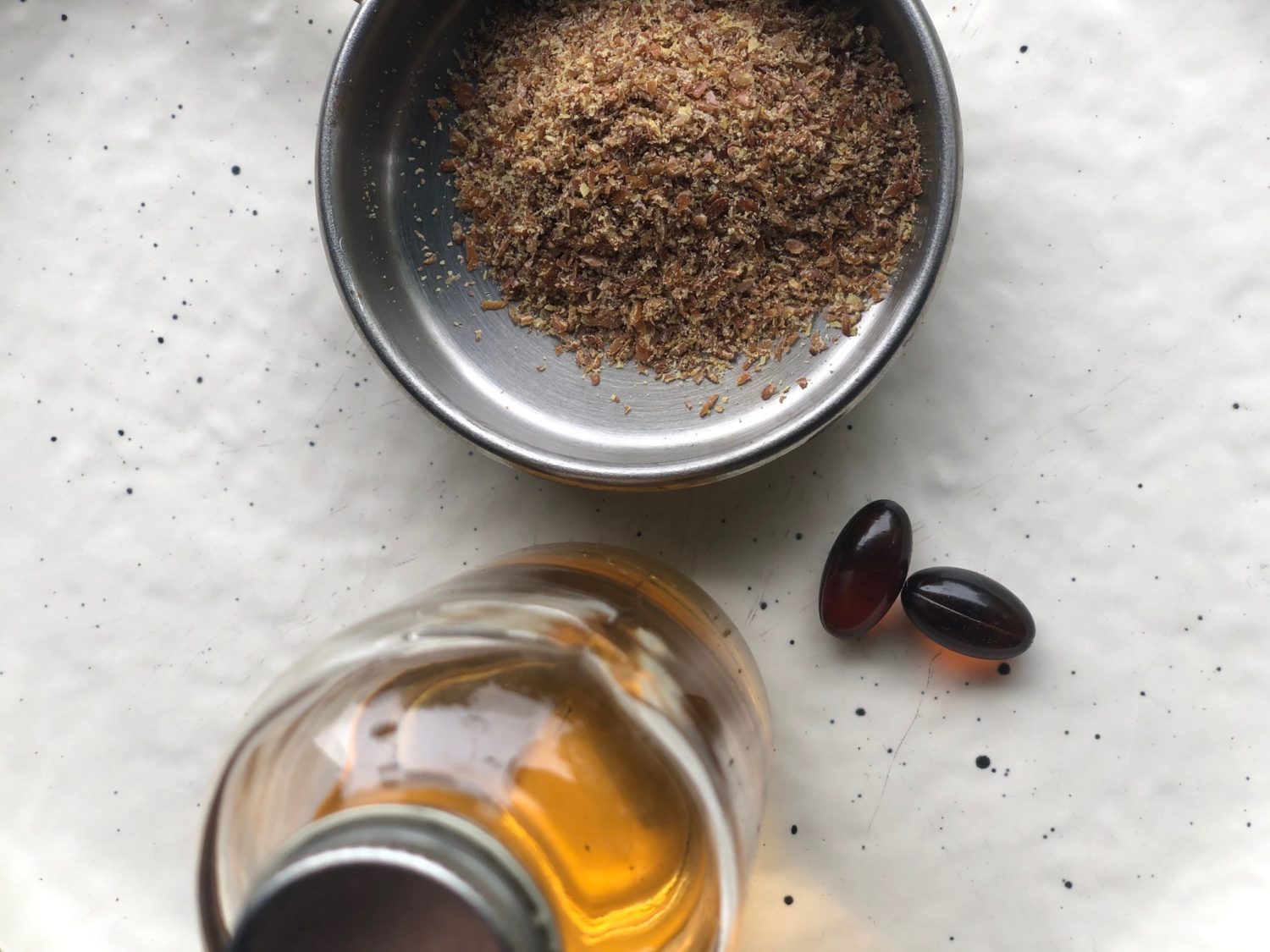 A Vivacity Acupuncture photograph showing various ways to consume Omega-3 essential oils from flax: as a liquid oil (bottom left), as softgel capsules (center right) and as a ground seed meal (center top).