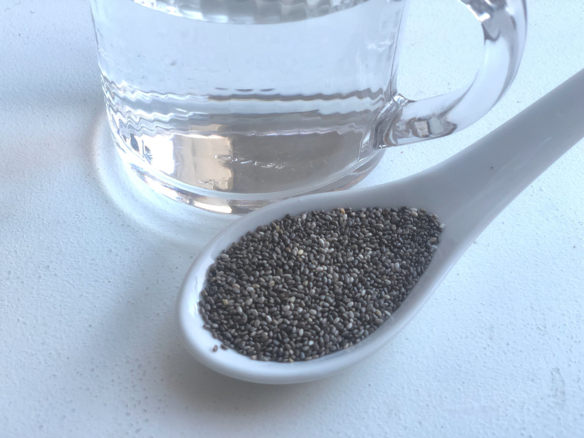 A spoonful of hydrophilic chia seeds next to a glass of water